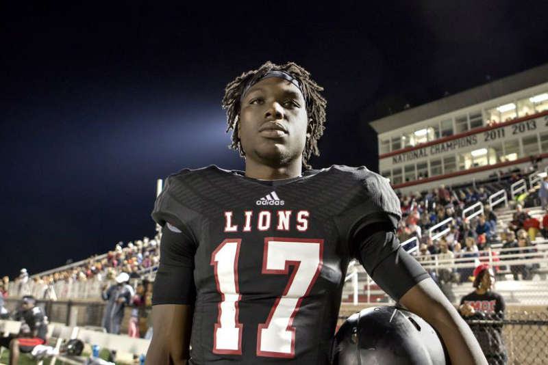 A football player holds a helmet on the sideline.