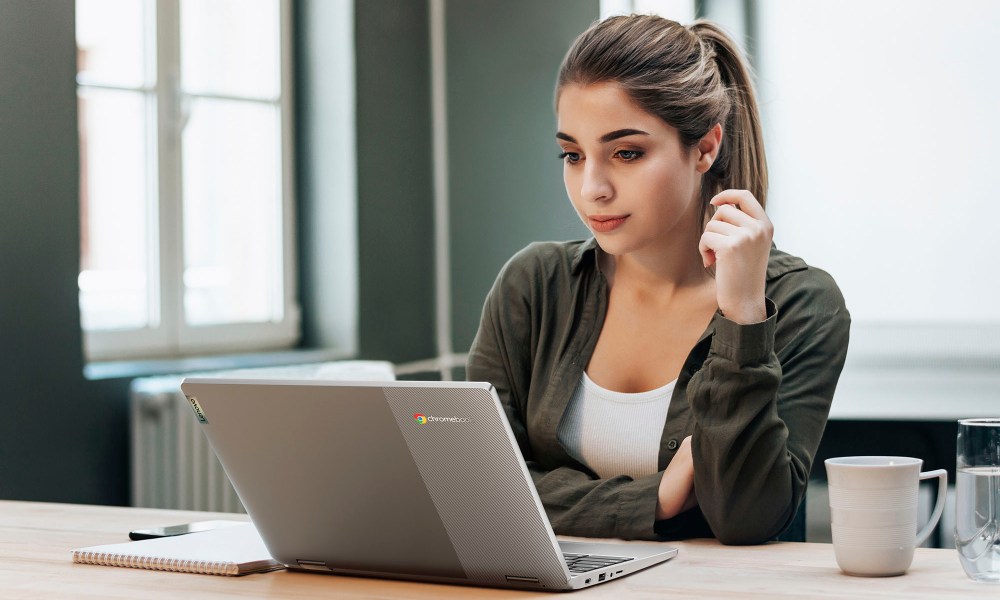 A woman sitting in front of an open Chromebook laptop.