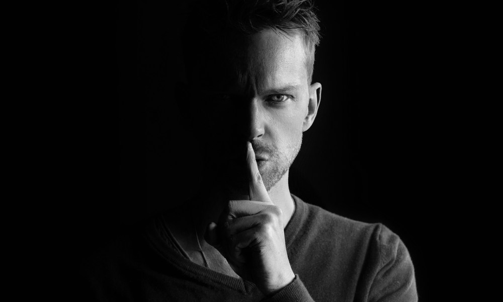 Man holding a finger to his lips depicting a secret.