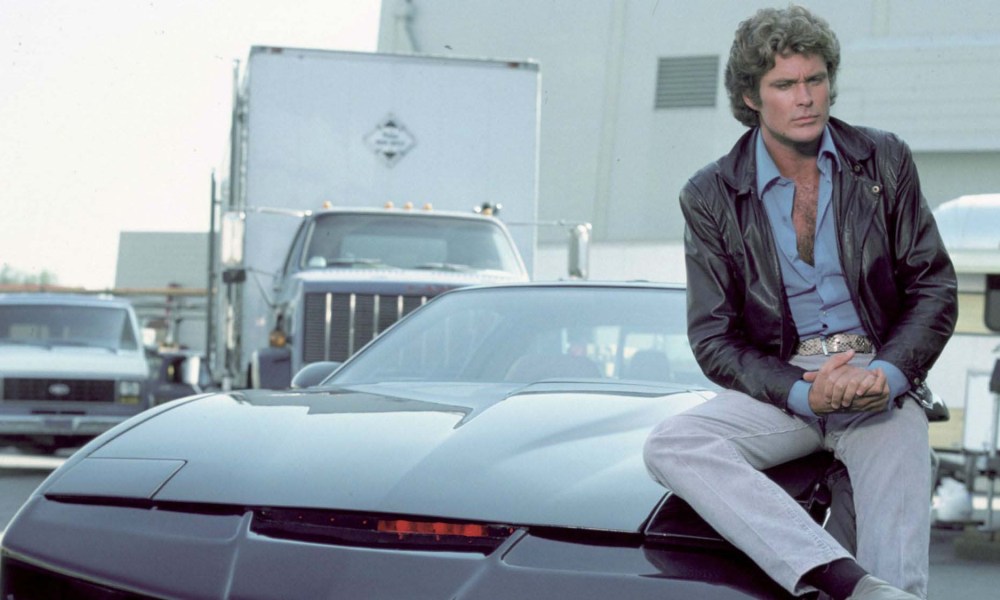 Michael Knight sitting on the hood of his car KITT in a scene from Knight Rider.