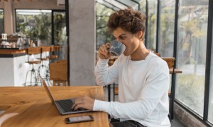 A person drinking coffee while using a laptop at a table.