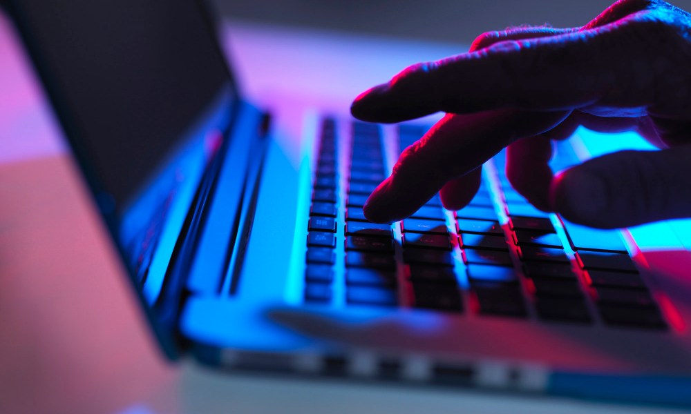 Silhouette of male hand typing on laptop keyboard at night.