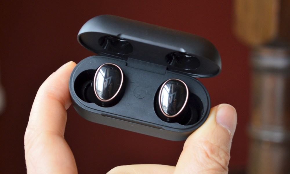 A hand holding the 1More Evo earbuds in their charging case.