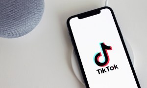 A smartphone and two other devices on a white table. The smartphone has the TikTok logo on its screen.