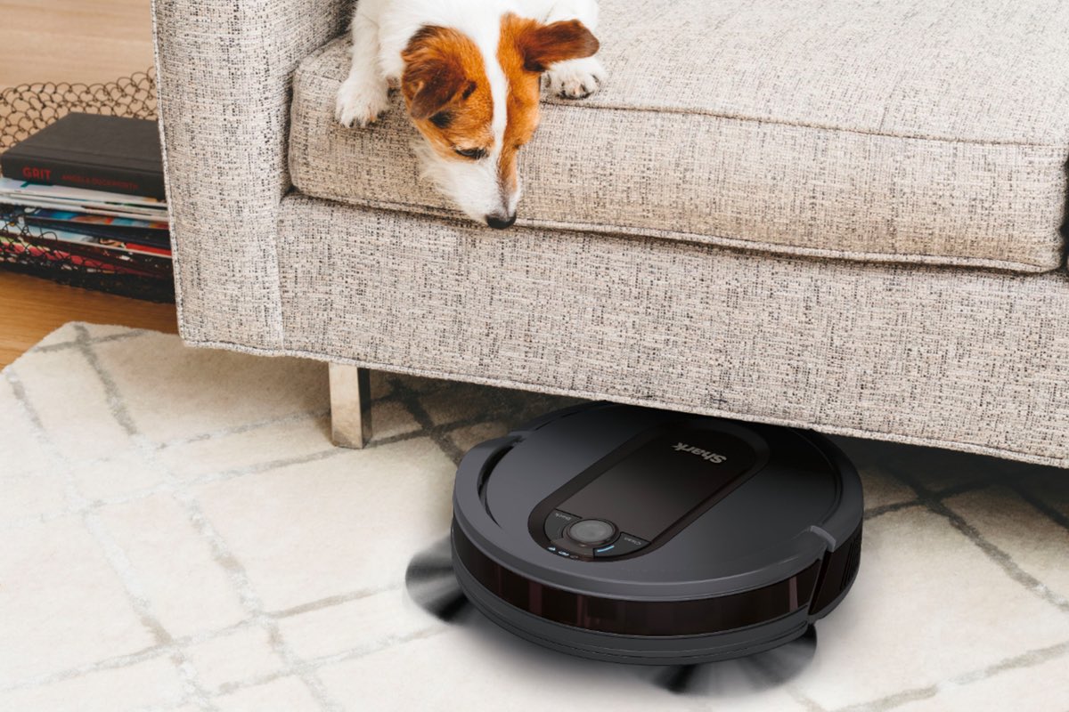 A Shark EZ robot vacuum cleans up under a couch.