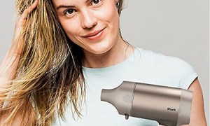 A woman wearing a white t-shirt uses the Shark HyperAir Hair Dryer to blow dry her hair.