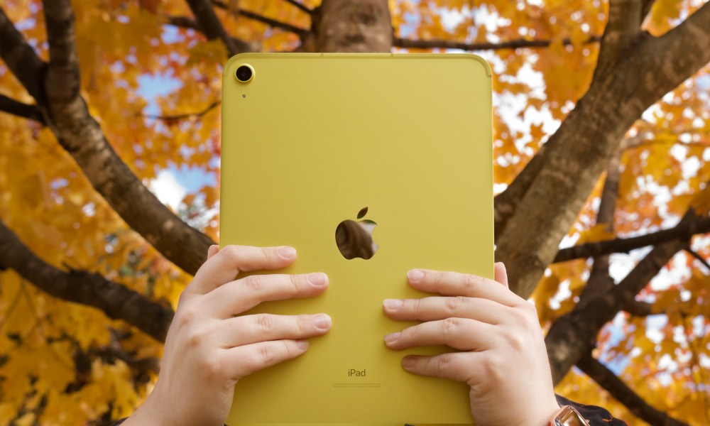 Someone holding the yellow iPad (2022) in front of trees with orange, yellow leaves.