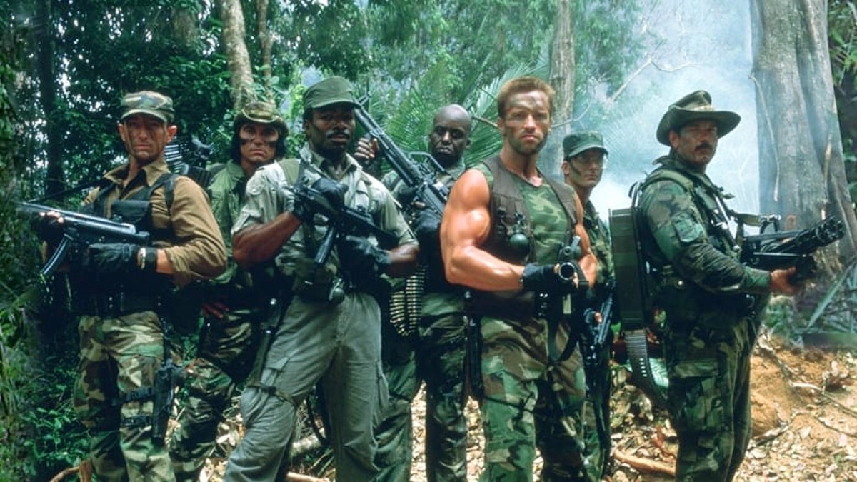 The cast of Predator poses with their guns in the jungle.