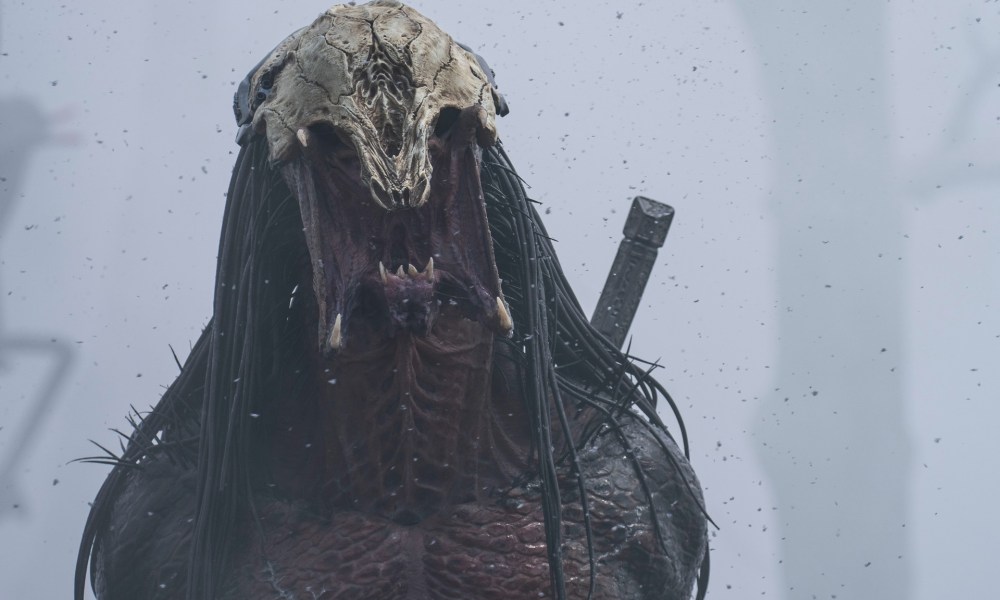 The Predator alien roars against a gray fog in the background.