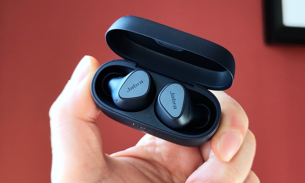 Jabra Elite 4 in an open charging case held by a hand.