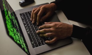 A person using a laptop with a set of code seen on the display.