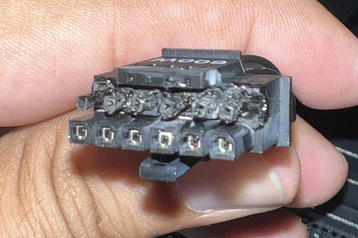A person holds the connectors of an Nvidia 12VHPWR cable from an RTX 4090 graphics card. The ends of the connectors are burned a