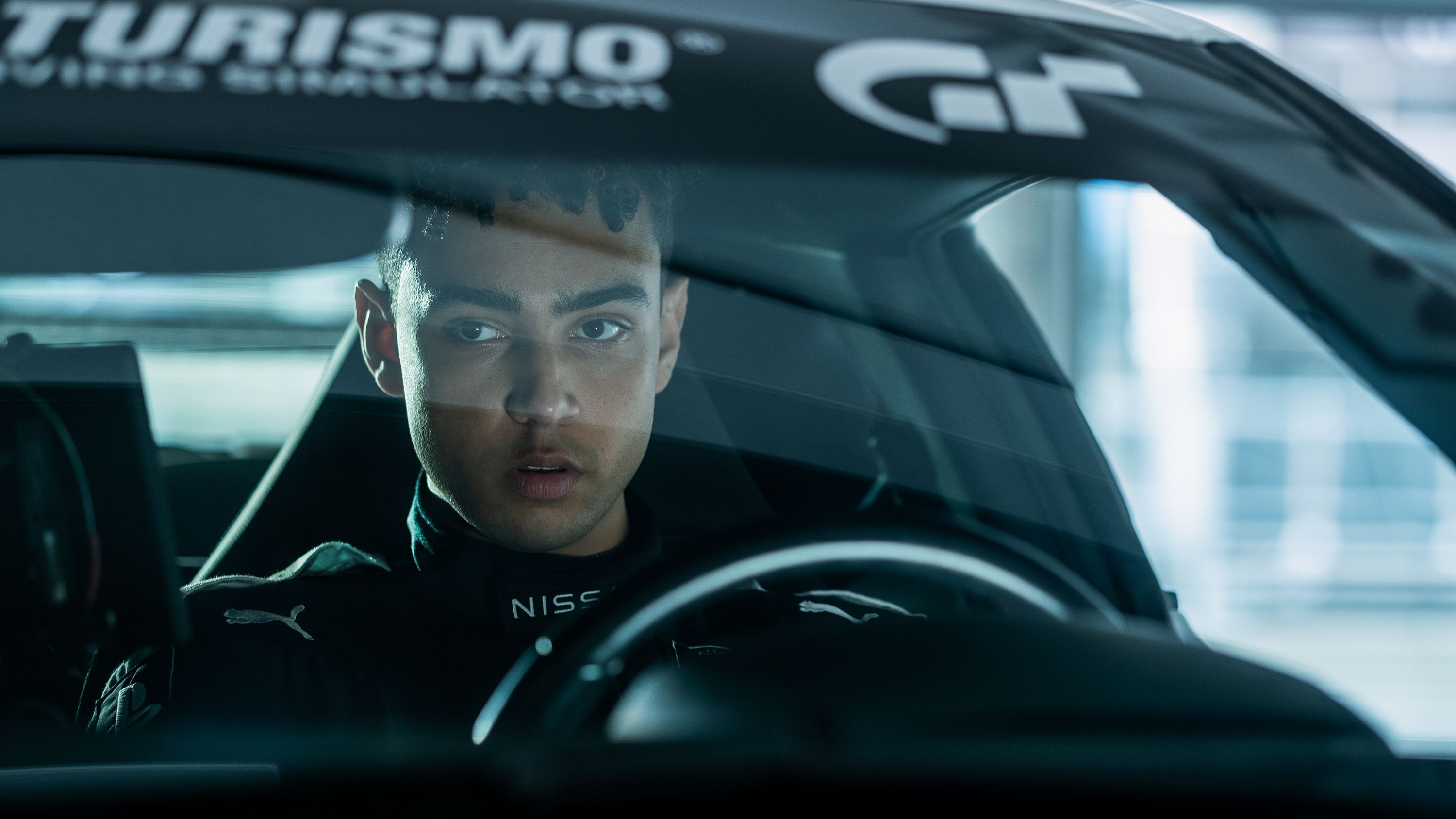 Archie Madekwe sits behind the wheel of a race car.