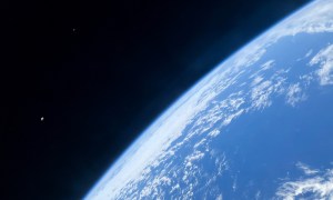 A photo taken from a SpaceX Crew Dragon showing Earth, the moon, and the space station.