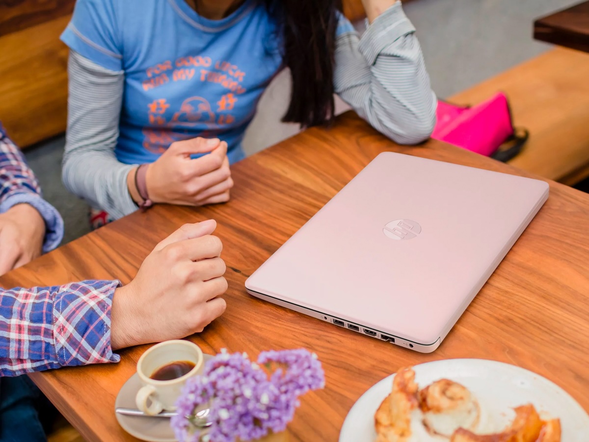 A pink model of the HP Stream 14-inch laptop sets on a café table while people converse.