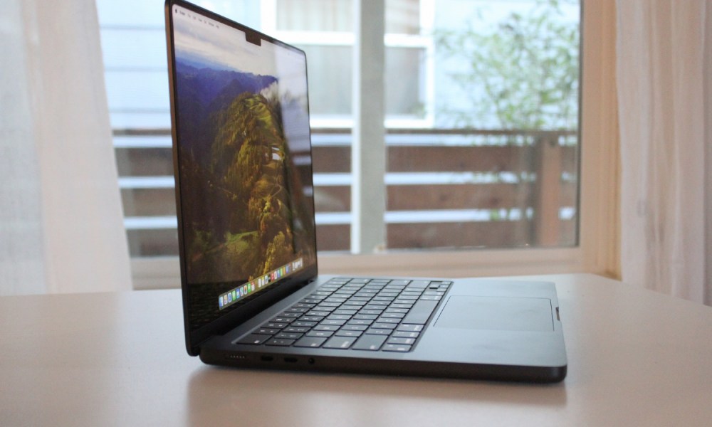 A MacBook Pro on a table in front of a window.