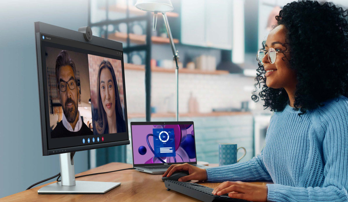 A woman using a laptop connected to a Dell 24 video conferencing monitor.