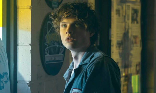 Sam wearing a mechanic's uniform in a garage looking scared while standing by a window in a scene from Gen V.