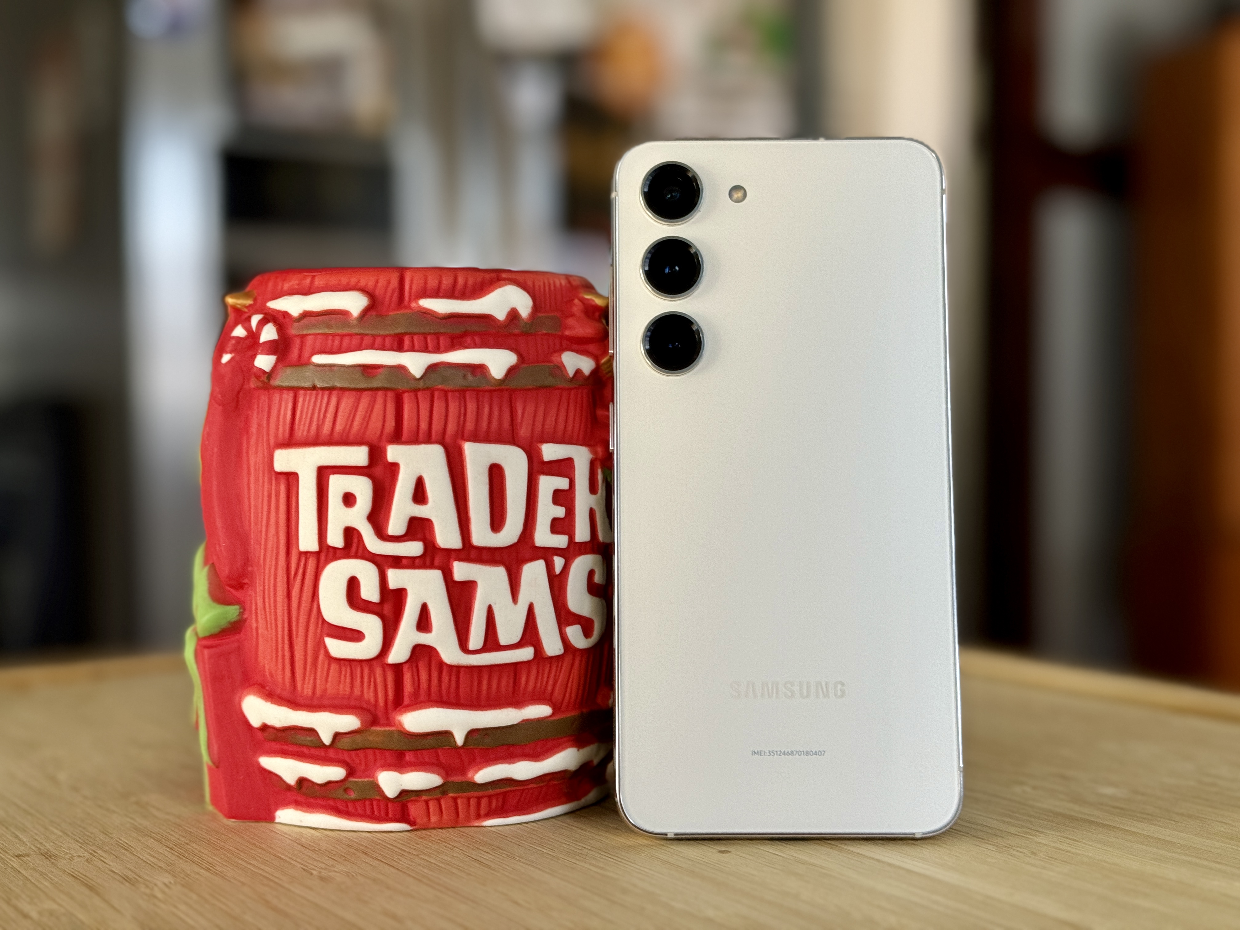 Samsung Galaxy S23 in cream standing next to a Trader Sam's christmas yule tiki mug.