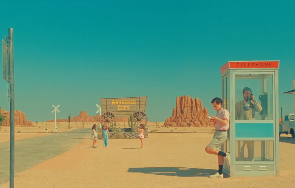 A boy leans on a phone booth in Asteroid City.