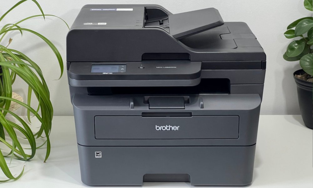 Brother's MFC-L2820DWXL laser printer rests on a white table with plants.