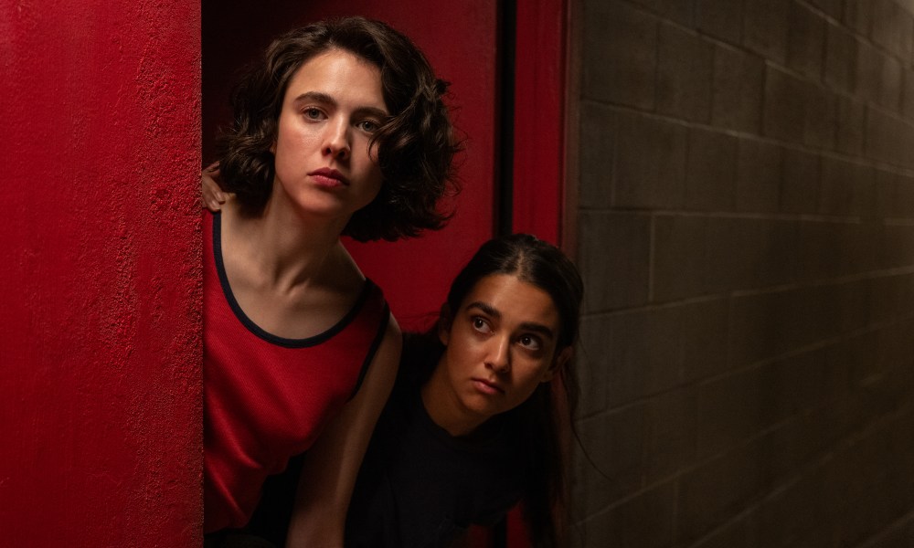 Margaret Qualley and Geraldine Viswanathan peer around a corner in a still from Drive Away Dolls