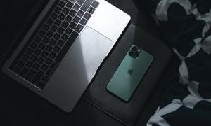 A MacBook and iPhone in shadow on a surface.