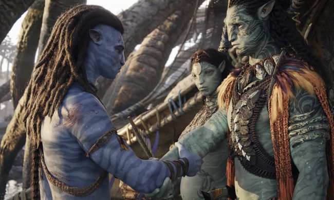 A Na'vi shakes hands with another man as a woman looks on.