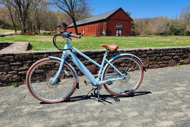 Priority Bicycles e-Classic Plus e-bike left profile shot parked on crushed stone in front of a stone wall with a red converted barn in the background.