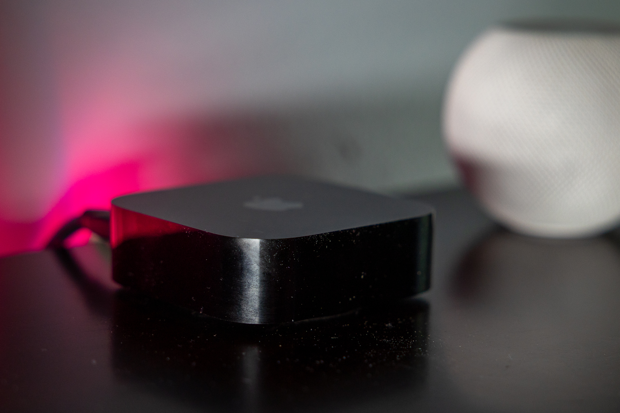 An Apple TV 4K sitting on a wood entertainment center with a HomePod Mini behind it.