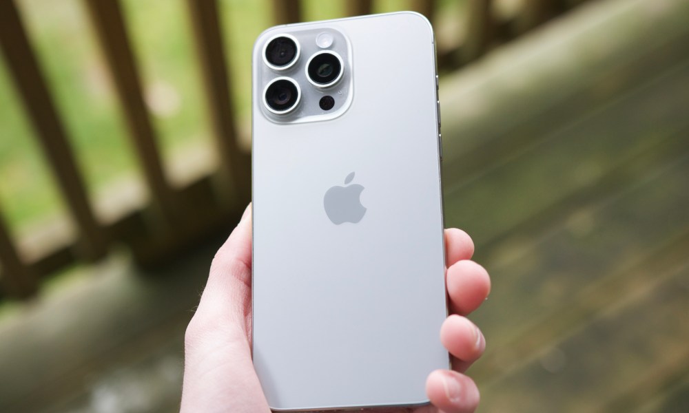 Someone holding an iPhone 15 Pro Max outside on a patio, showing the back of the Natural Titanium color.