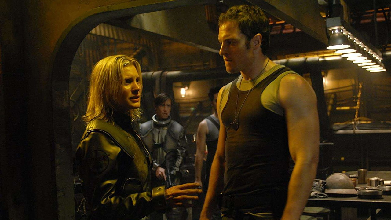 A woman talking to a man in a tank top on a ship in a scene from Battlestar Galactica.