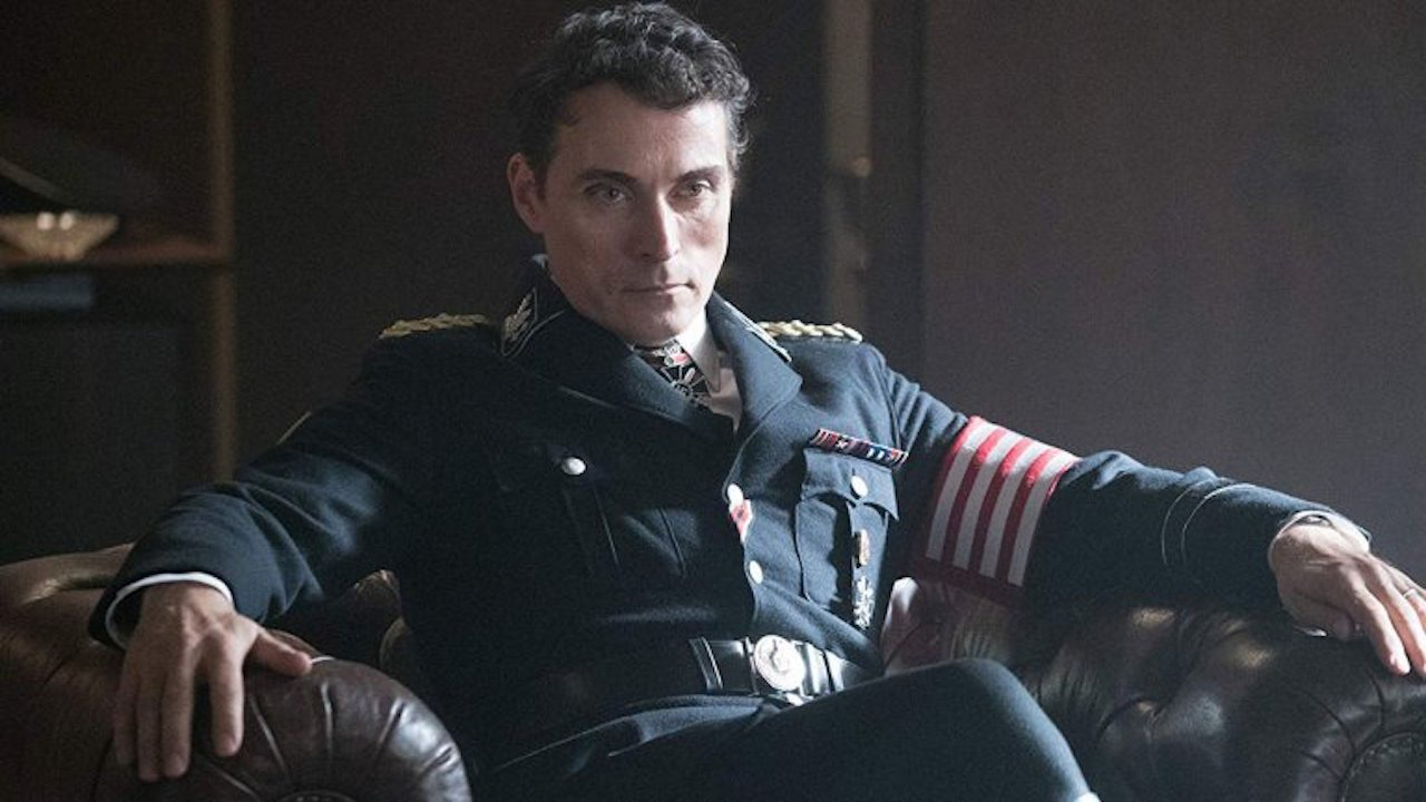 A man sitting back in a chair with an army uniform, looking serious in The Man in the High Castle.
