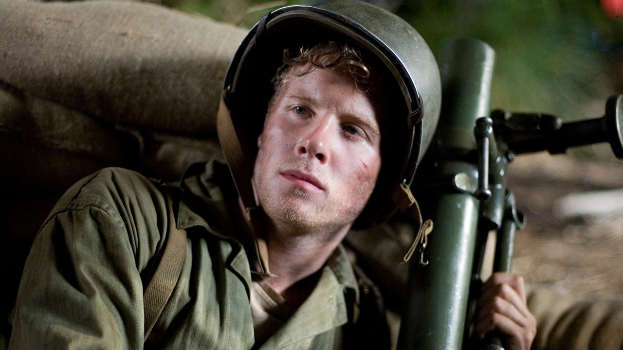 A man in army wear lying down, a gun in his hand in a scene from The Pacific.