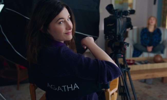 A woman sits in a director's chair and turns back to the camera.