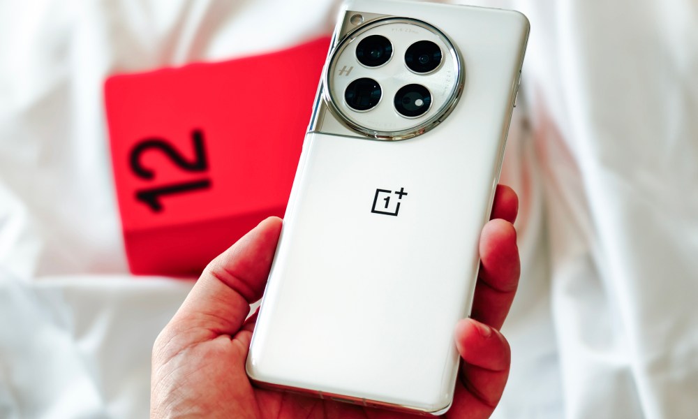 OnePlus 12 Glacial White color held in hand against its red box.