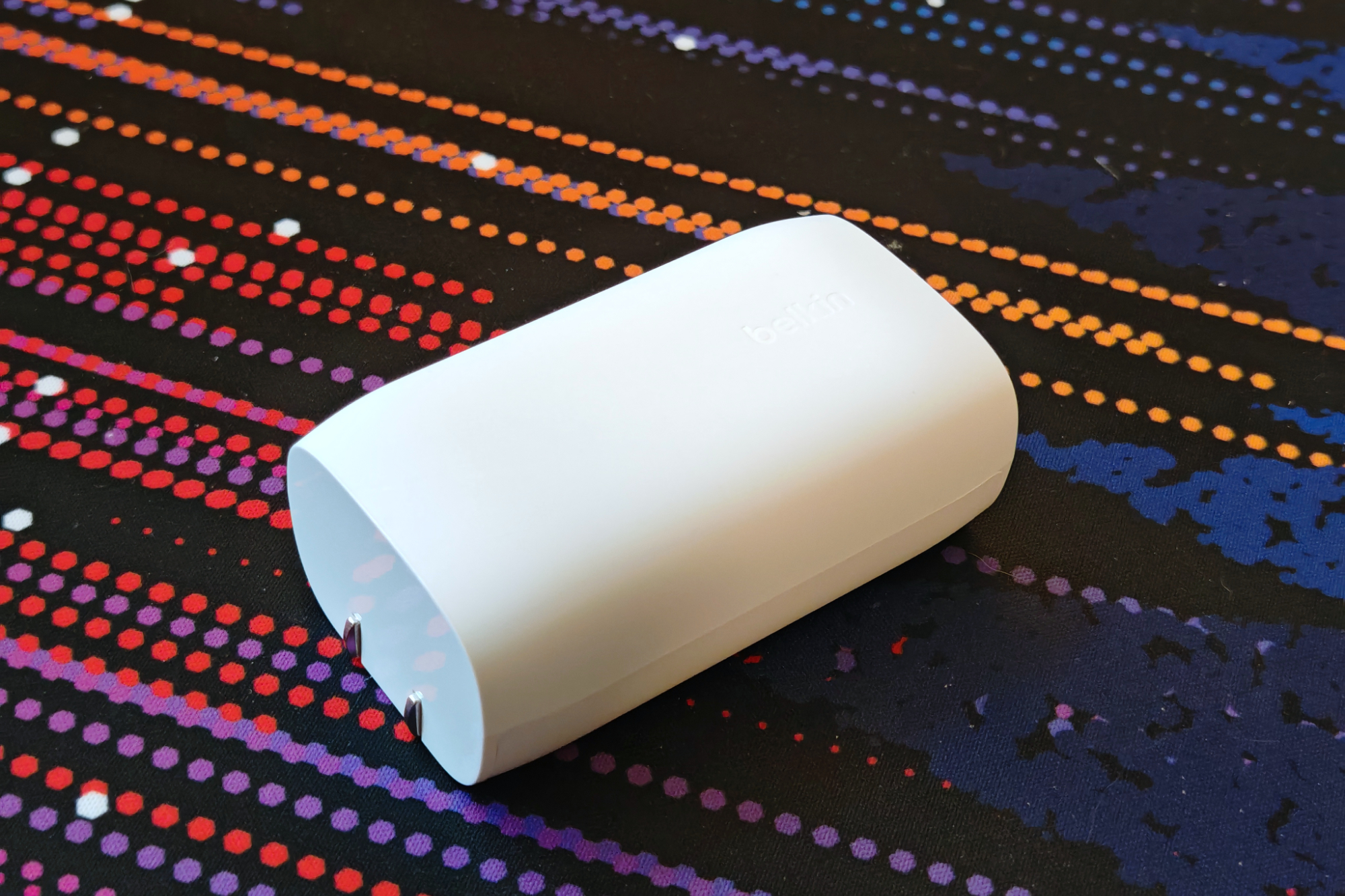 A white Belkin charger laying on a colorful desk mat.