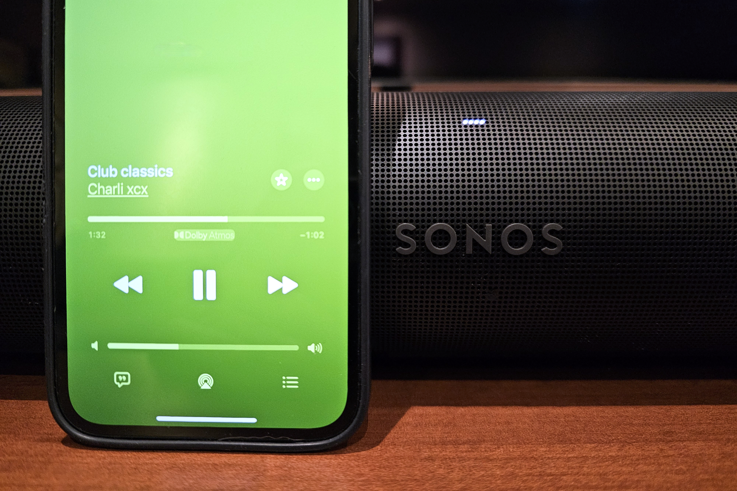 An iPhone playing Dolby Atmos Music from Apple Music sitting in front of a Sonos Arc soundbar.