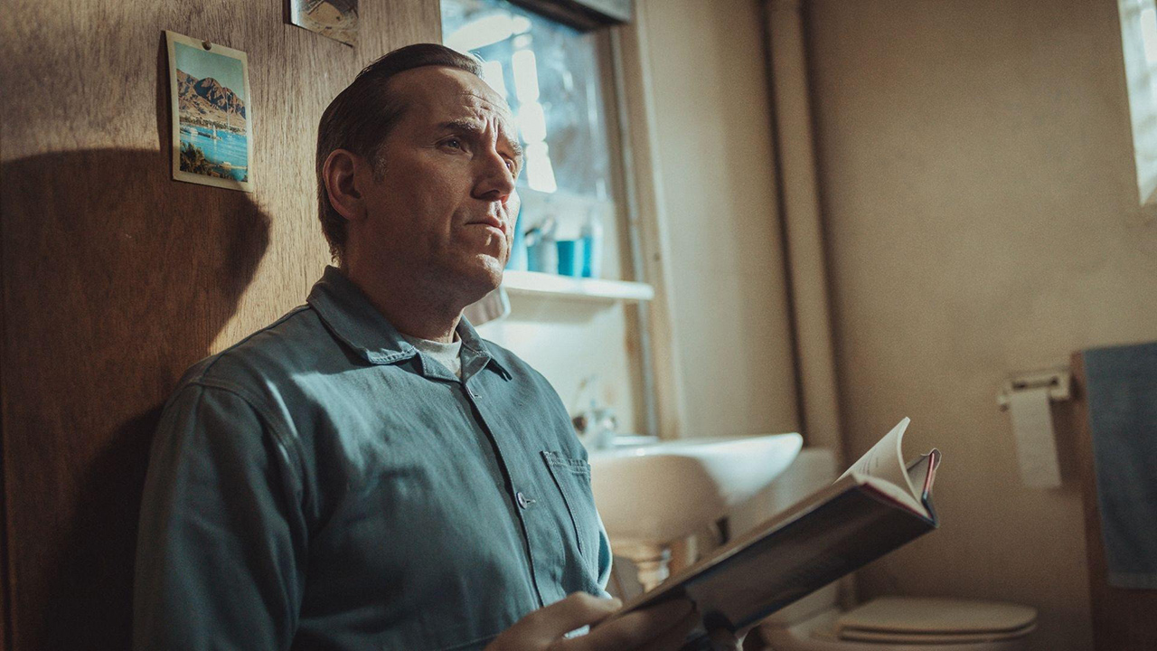 A man holding a book while looking up and pondering in a scene from Professor T.