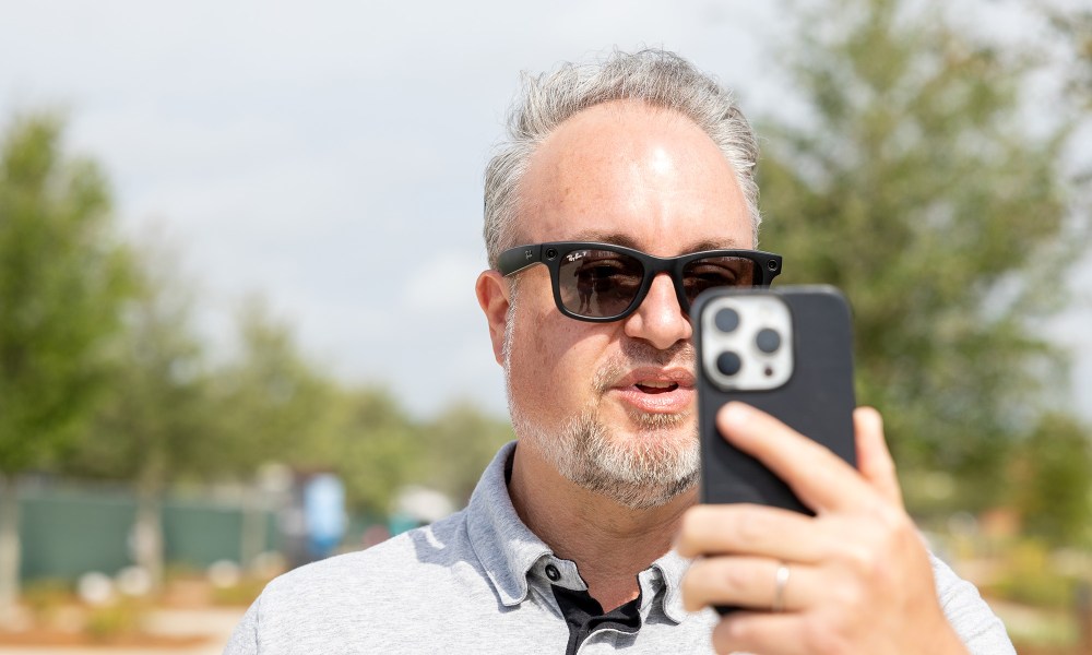 Phil Nickinson wearing the Ray-Ban Meta smart glasses while talking into an iPhone.