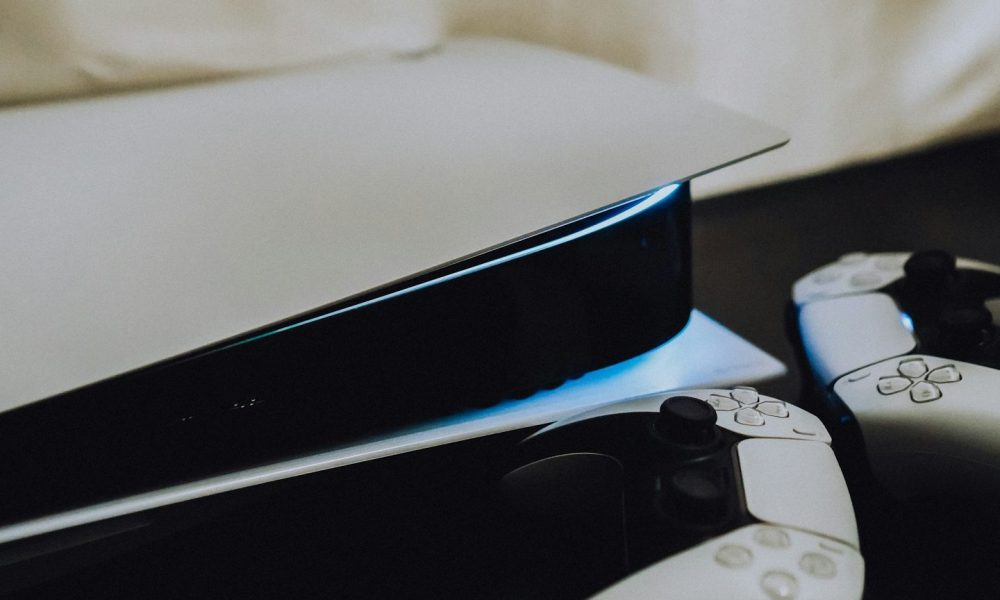 A PS5 sitting on its side with two Dualsense controllers next to it on the right.