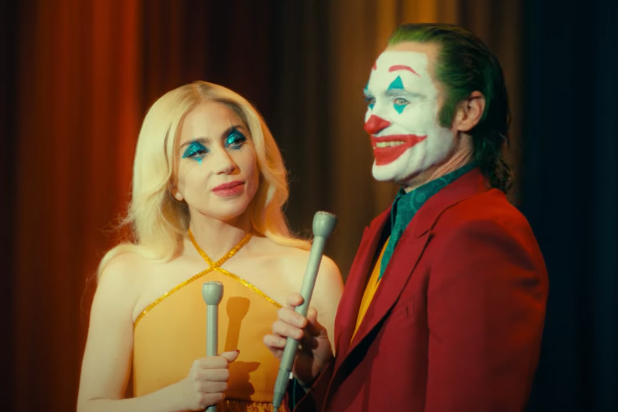 Lady Gaga and Joaquin Phoenix hold mics and smile in Joker 2.