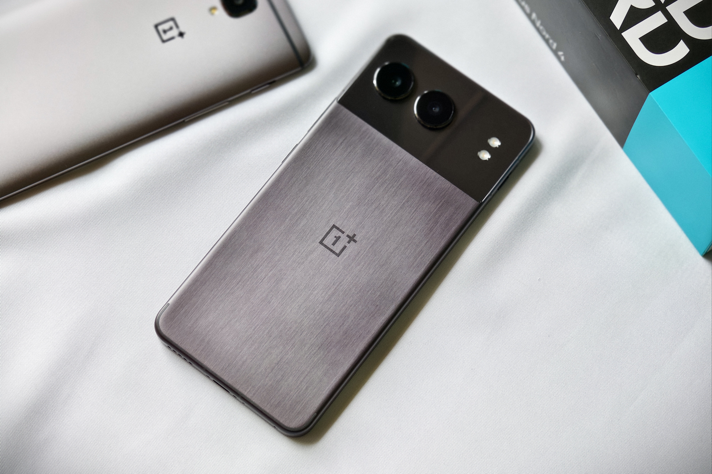 OnePlus Nord 4 in midnight black color with a metal unibody shell kept on a white fabric beside a gunmetal OnePlus 3T.