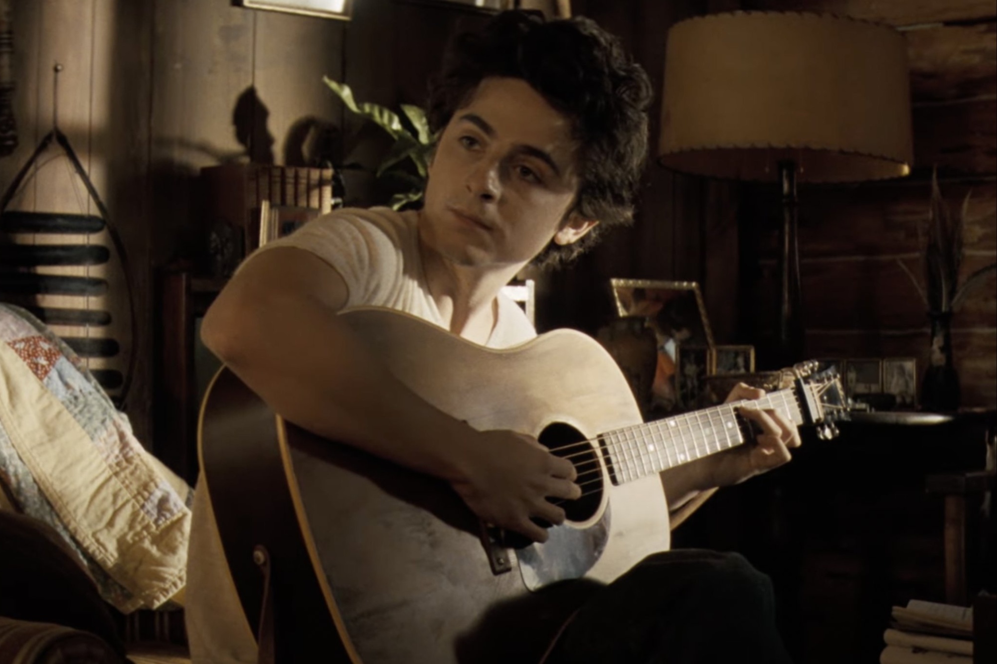 Timothee Chalamet holds a guitar and stares in A Complete Unknown.