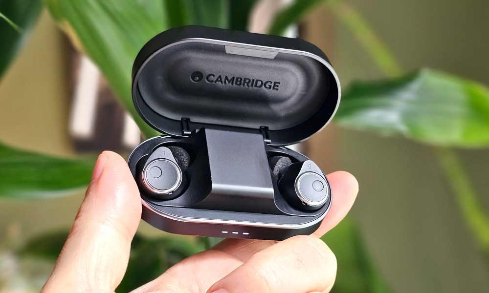 Cambridge Audio Melomania M100 in charging case, lid open, held in hand.