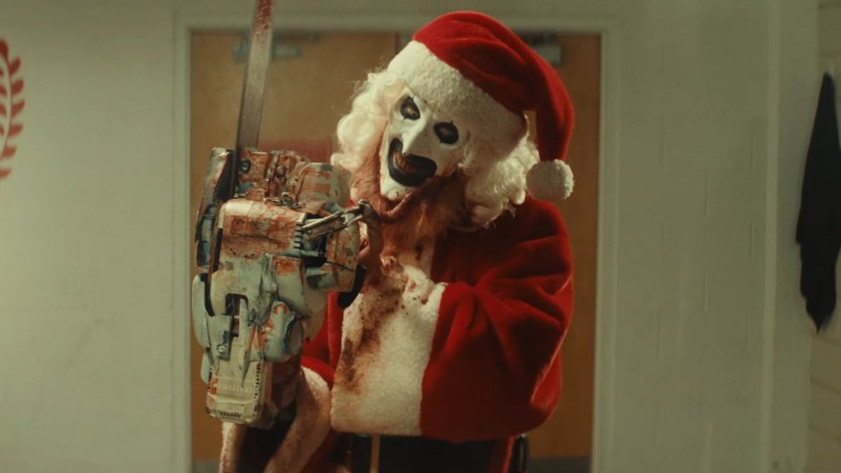 Art the Clown dressed as Santa holds a chainsaw in Terrifier 3.