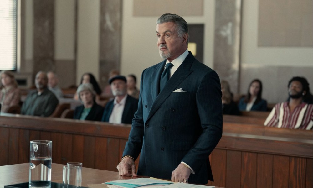 Sylvester Stallone stands up in front of a table in Tulsa King.