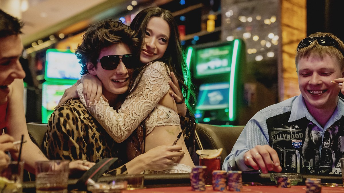 A woman sits on a man at a poker table in Anora.