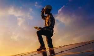 Promotional image for Tech For Change. Person standing on solar panel looking at sunset.