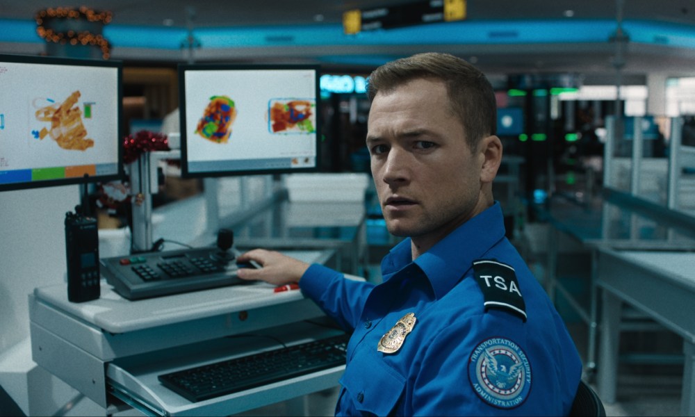 Taron Egerton sits at a desk and looks back in Carry-On.